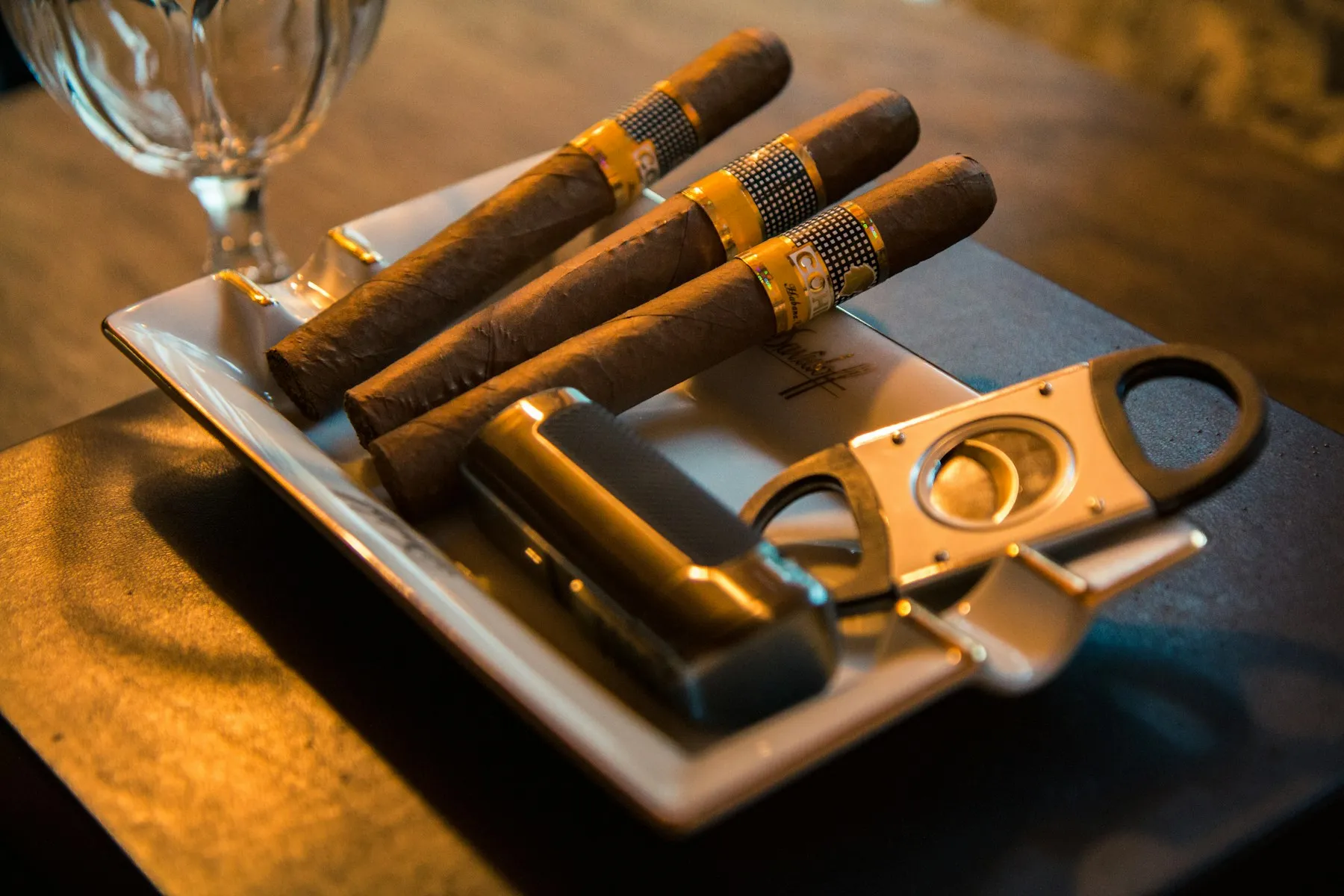 Three hand-rolled cigars resting beside a cutter on a stone ashtray