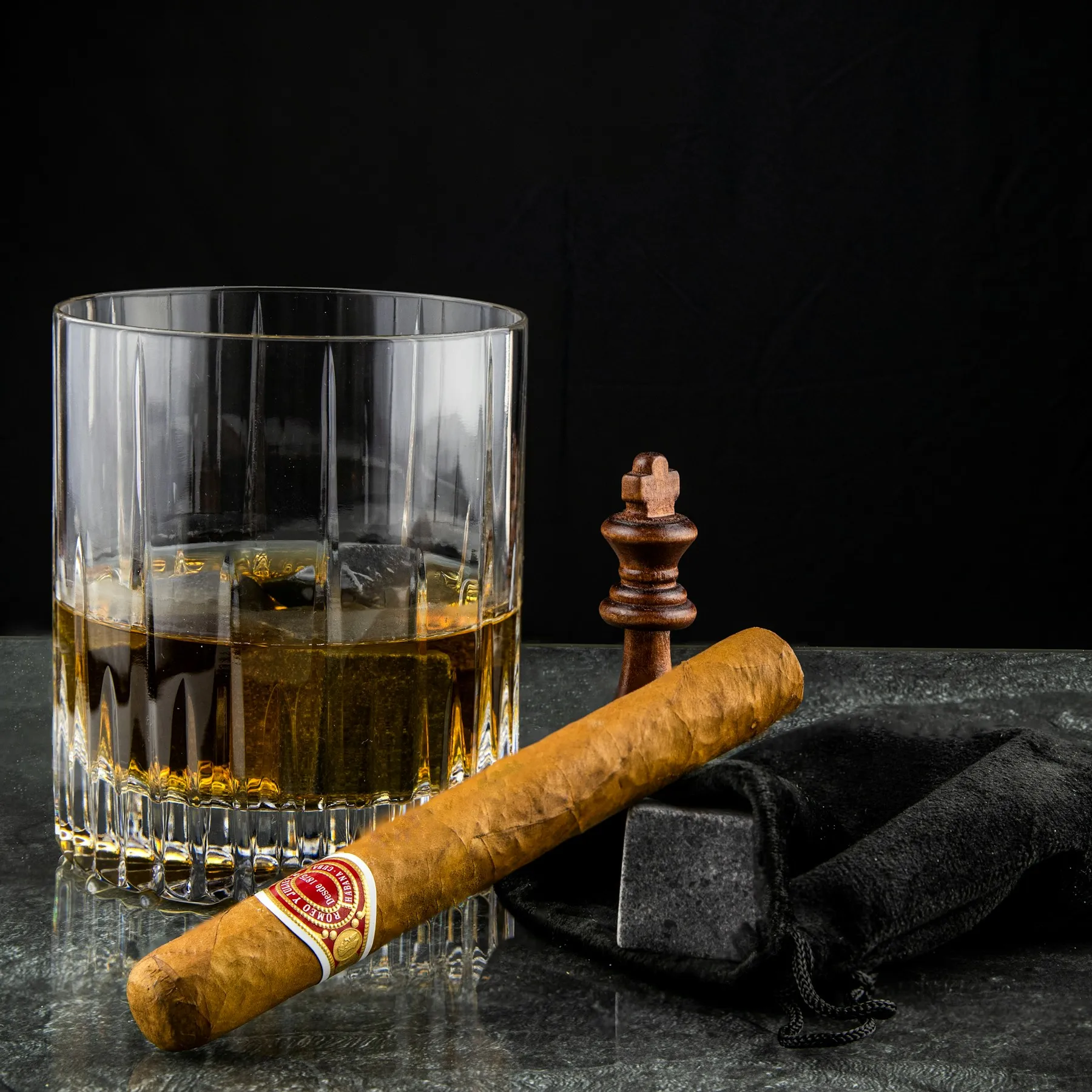 A glass of whiskey beside a lit cigar on a wooden table
